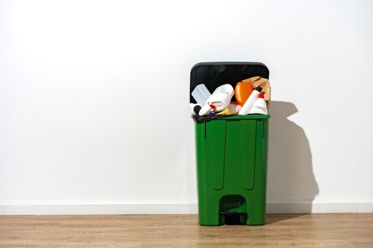 Green plastic trash can full of garbage indoors